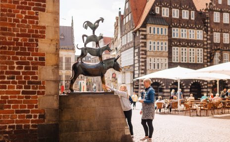 Ein Mädchen und eine Frau stehen vor den Bremer Stadtmusikanten.