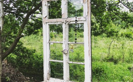 Ein Fenster mit weißem Fensterrahmen ist an einem Baum über einer grünen Wiese aufgehängt.