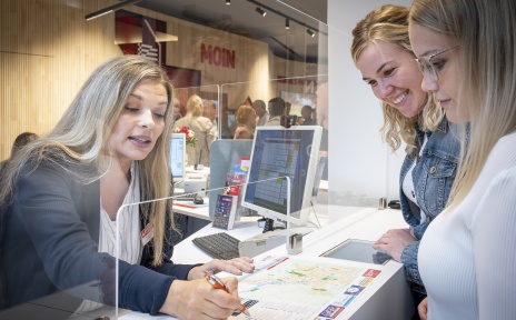 A woman stands behind a counter and shows two other women something on a city map.