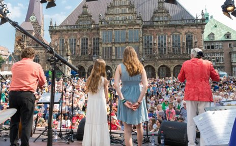 Auf der Bühne vorm Domshof stehen mehrere Musiker*innen und singen. 