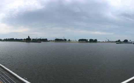 Zu sehen ist eine große, dunkle Wasserfläche. Im rechten und linken Teil des Bildes ist ein Metallgeländer zu erkennen. Links legt ein Boot an. 