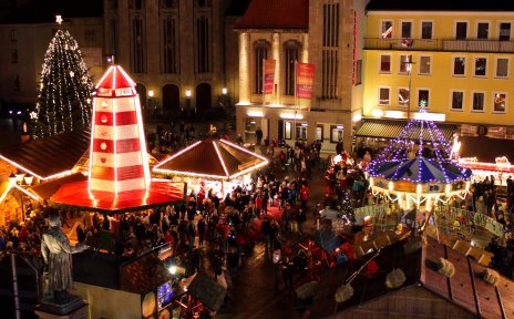 Ein Weihnachtsmarkt mit beleuchteten Buden und vielen Menschen aus der Vogelperspektive.