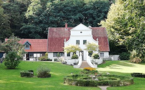 Ein großer, aufwendig angelegter grüner Garten. Im Hintergrund ist ein weißes Haus im Jugendstil zu sehen, der Barkenhoff in Worpswede.