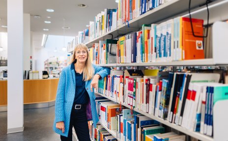 Eine Frau lehnt sich an einem Regal in einer Bibliothek an