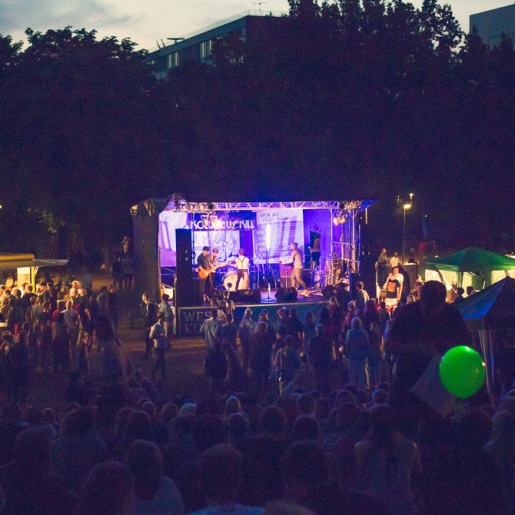 Eine Bühne mit Band und Publikum im Sommer, draußen im Dunklen.