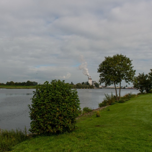 Ein Blick vom Ufer auf die Weser, im Hintergrund raucht der Schornstein eines Unternehmens.