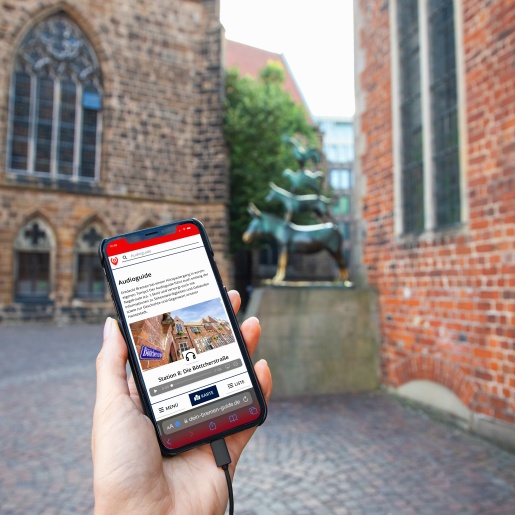 Someone is holding a smartphone with the audio guide open. The Bremen Town Musicians are in the background.