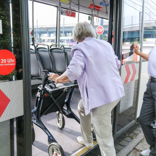 Eine ältere Dame mit Rollator steigt in einen Bus ein. Eine Mitarbeiterin der BSAG begleitet sie dabei.