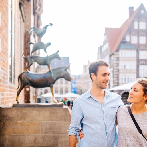 Eine Frau und ein Mann stehen vor den Bremer Stadtmusikanten. 