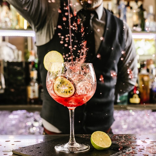 Ein Barkeeper gießt aus größerer Entfernung Flüssigkeit in ein Cocktailglas