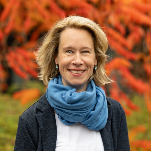 Eine Frau steht lachend vor einer Hecke in herbstlichen Farben