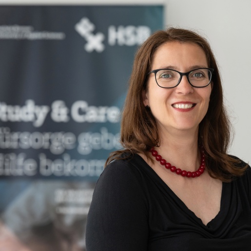 Ein Frau blickt lachend in die Kamera. Sie hat lange dunkle Haare und eine rote Kette.