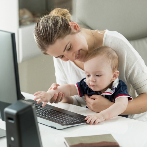Eine lächelnde Frau sitzt mit einem Kleinkind am Computer.