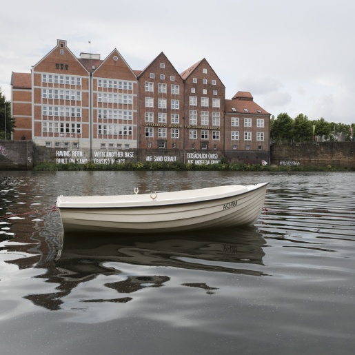 Im Vordergrund ein kleines weißes Boot mit Namen Achim auf der Weser, im Hintergrund die Weserburg