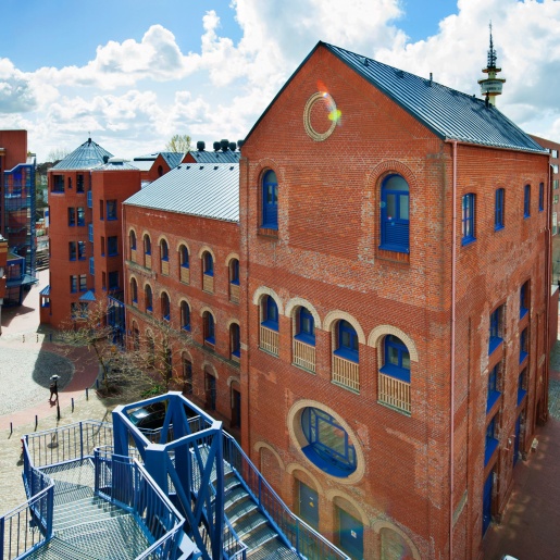 Ein rotes Backsteingebäude, im Vordergrund eine große blaue Metalltreppe; Quelle: Thilo Vogel