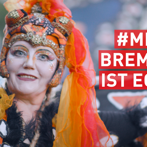 Eine Frau in einem bunten Schmetterlings-Kostüm und mit bunter Schminke lächelt in die Kamera. Rechts im Bild steht in weißer Schrift auf rotem Untergrund: "#Mein Bremen ist echt".