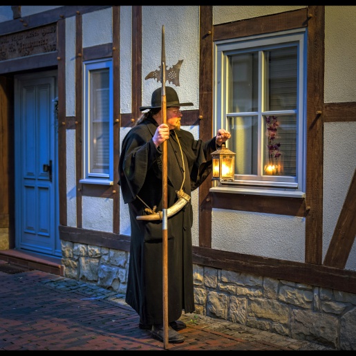 Ein als Nachtwächter verkleideter Stadtführer vor einem alten Fachwerkhaus