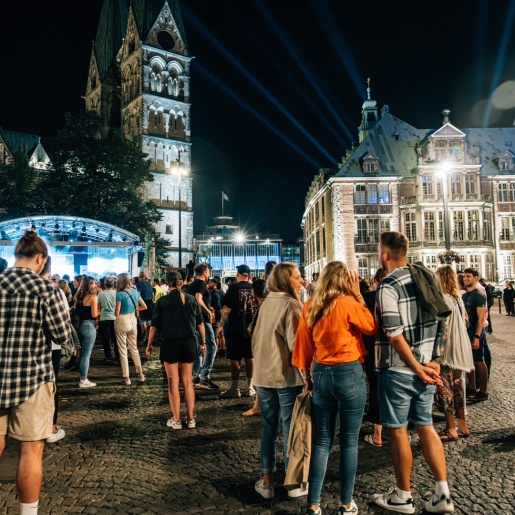 Groups of people stand in front of a large stage at night on the Domshof in Bremen.