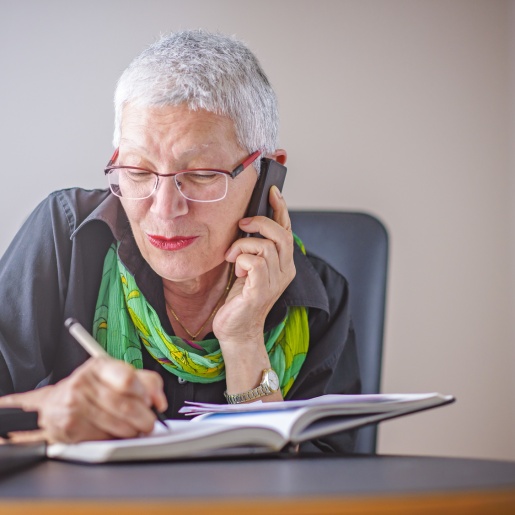 Eine Seniorin schreibt etwas in eine Notizbuch, während sie telefoniert.