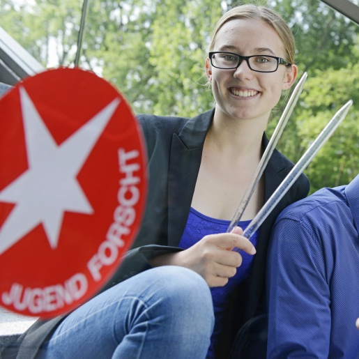 Ein junger Mann und eine junge Frau mit Forschungsgeräten neben dem Jugend forscht Logo