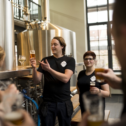 Ein Mitarbeiter und eine Mitarbeiterin der Union Brauerei führen eine Brauereiführung für Gäste durch.