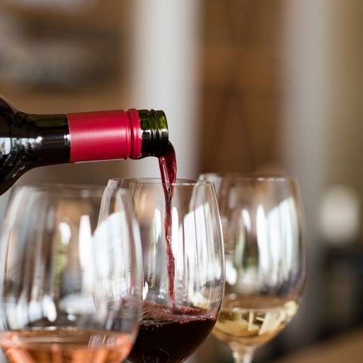 Drei gefüllte Weingläser, eine Flasche gießt Rotwein in eines der Gläser.