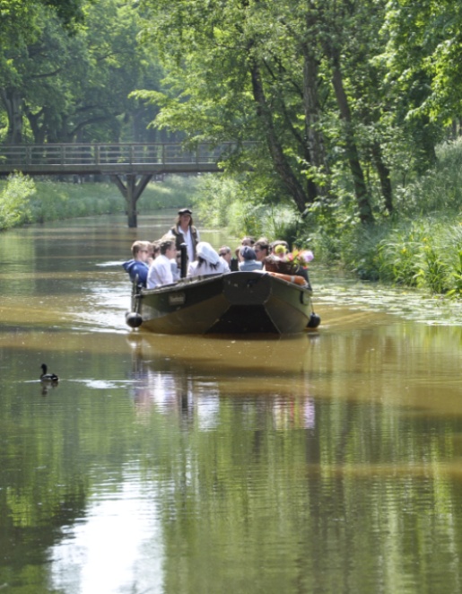 Eine Gruppe Menschen fährt mit einem Torfkahn einen Fluss entlang