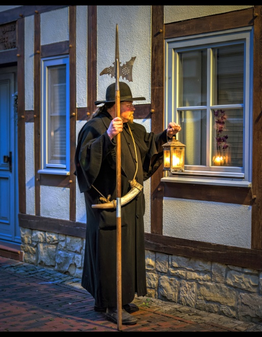 Ein als Nachtwächter verkleideter Stadtführer vor einem alten Fachwerkhaus