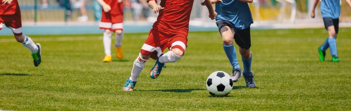 Personen in roten und blauen Trikots spielen Fußball. Ihre Köpfe sind nicht auf dem Bild zu sehen. 