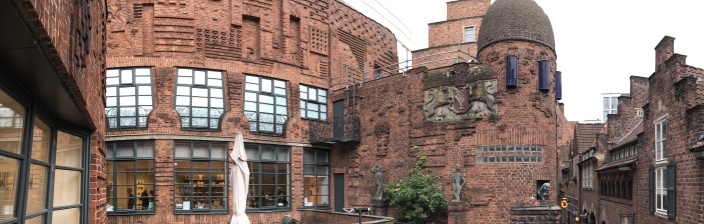Die rotbraune Außenfassade der Museen Böttcherstraße mit Terrasse und Kuppel. Auf der rechten Bildseite ist ein kleiner Teil der Gasse "Böttcherstraße" zu erkennen.