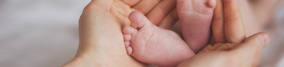 Die Hände einer Erwachsenen umfassen die Füße eines Babys