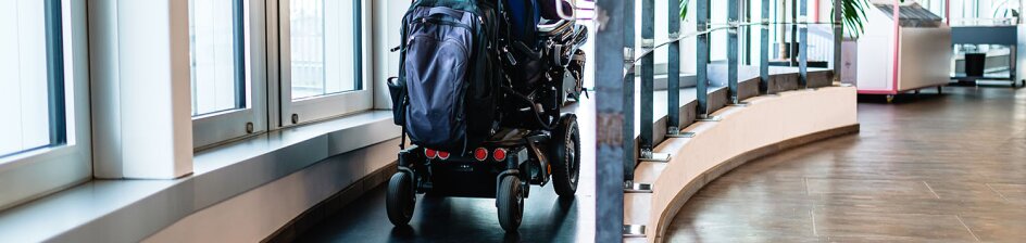 Eine Person im Rollstuhl fährt in einem Bürogebäude eine Rampe hoch.