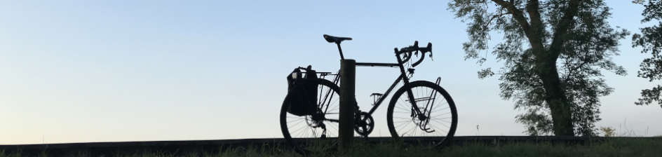 Ein Fahrrad steht auf einem Hügel abgestellt neben einem Baum vor blauem Himmel