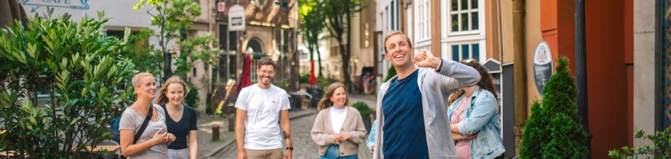 A man leads a group through the Schnoor district past small houses in a narrow alley.