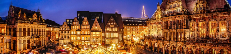 Eine historische Kulisse mit einem Weihnachtsmarkt, der in der Abendstimmung leuchtet.