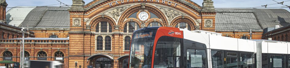 Eine Straßenbahn fährt um eine Kurve, dahinter der ein Bahnhof zu sehen.