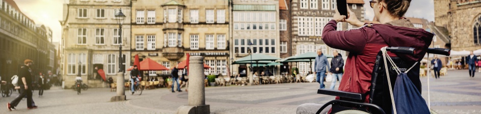 Eine Rollstuhlfahrerin macht Fotos auf dem Marktplatz.