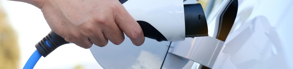 Ein Mensch steck ein Ladekabel in ein Elektrofahrzeug ein.