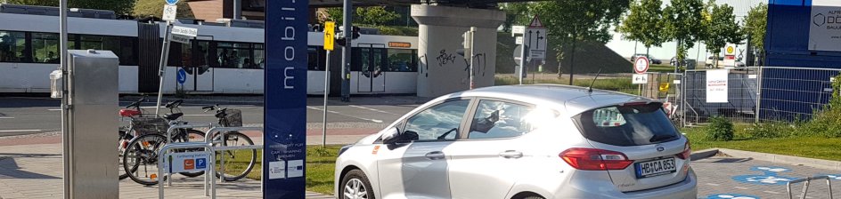 Ein Auto steht auf einem Parkplatz, im Hintergrund fährt eine Straßenbahn vorbei