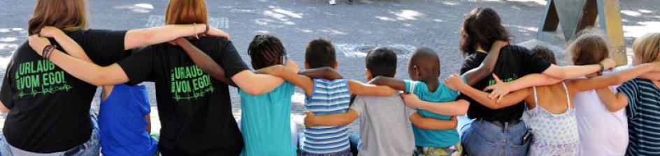 Kinder sitzen auf einer Mauer und haben einander die Arme um die Schultern gelegt.