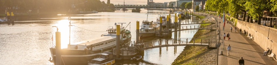 The "Schlachte" promenade on the Weser at sunset. There are numerous ships on the water. 