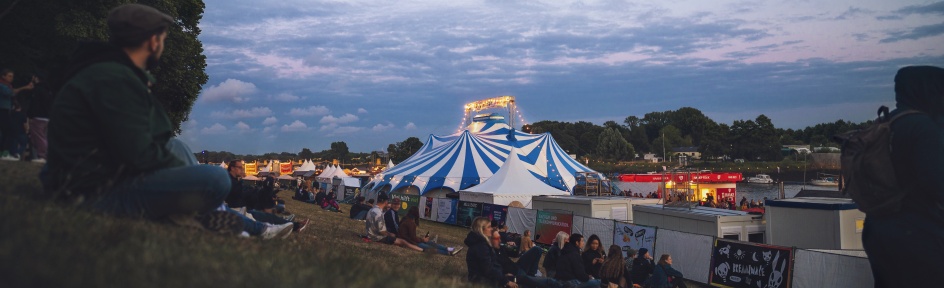 Menschen sitzen am Osterdeich in der Abenddämmerung und blicken aus die Festzelte der Breminale.