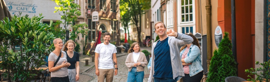 Ein Mann führt eine Gruppe durch das Schnoorviertel vorbei an kleinen Häusern in einer schmalen Gasse.