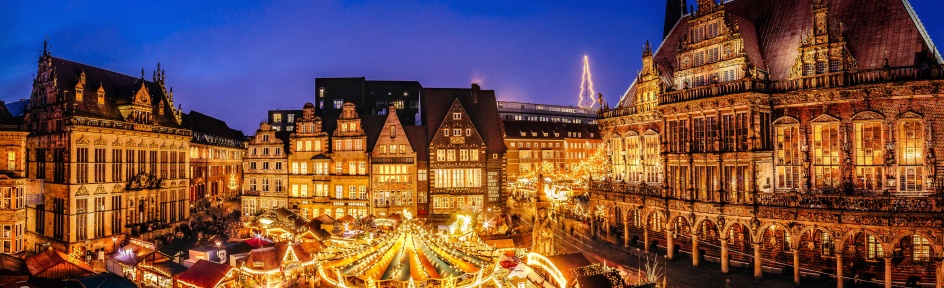 Eine historische Kulisse mit einem Weihnachtsmarkt, der in der Abendstimmung leuchtet.