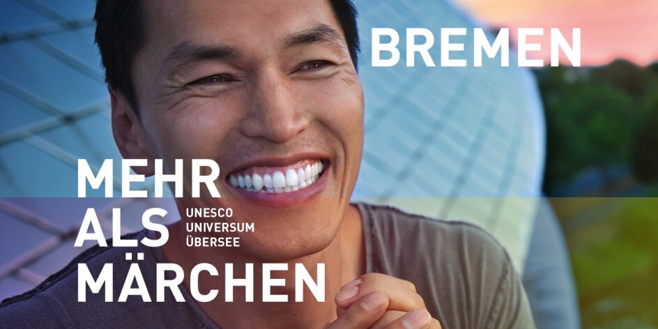 Ein lachender Mann vor dem Science Center Universum Bremen. Er hat schwarze Haare. Schriftzug im Bild: "Bremen - Mehr als Märchen. Unesco, Universum, Übersee". 