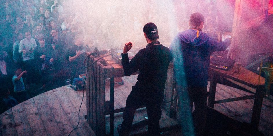 2 DJs stehen auf einer Bühne vor Publikum und legen auf. 