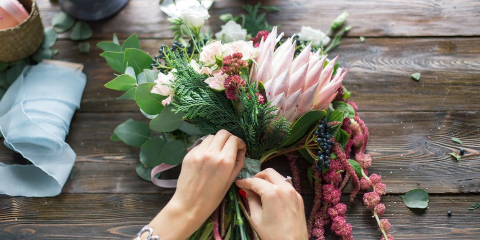 Frauenhände binden einen bunten Blumenstrauß zusammen.