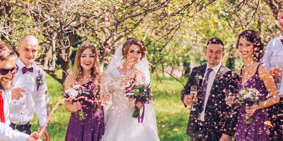 Ein Brautpaar steht mit seinen Gästen auf dem Rasen und lässt Konfetti regnen
