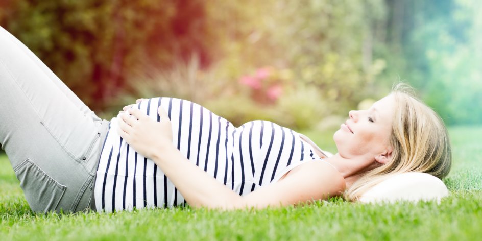 Eine schwangere Frau liegt lächelnd auf einer Wiese (Quelle: fotolia / drubig-photo)