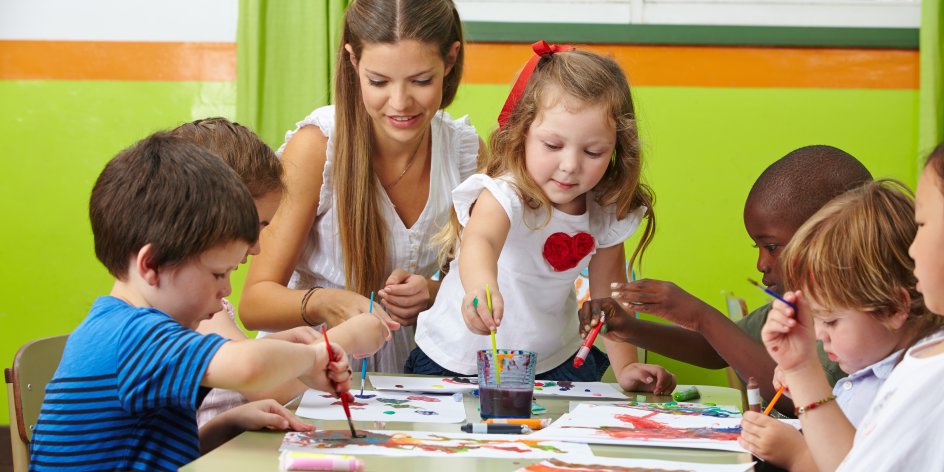 Kindergarten Kinder malen mit bunten Wasserfarben an ihren Bildern. Die Erzieherin macht auch mit. 
